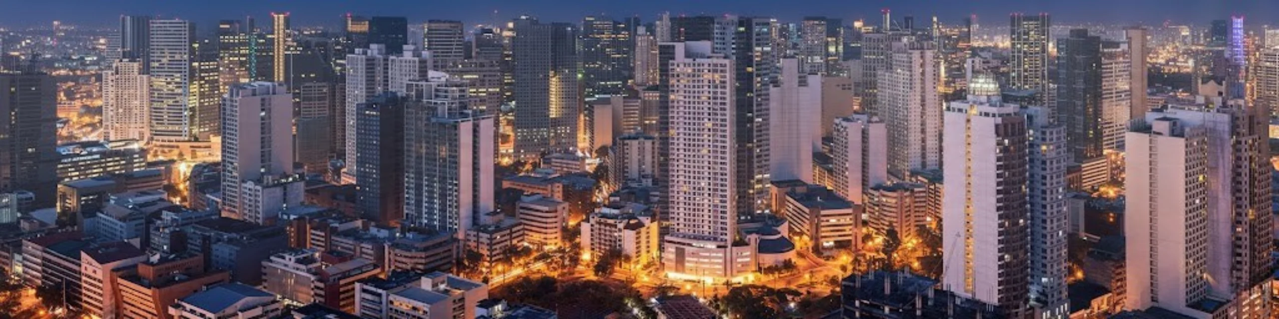 Panoramic night view of a dense metropolitan skyline featuring illuminated high-rise office buildings and urban apartment blocks.